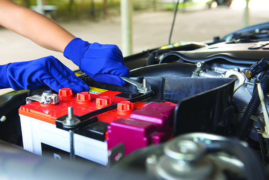 Mechanic wearing blue safety gloves tightening car battery terminals during service in Bonita Springs, FL