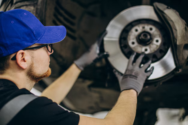 Auto technician in a blue cap inspecting a front brake rotor assembly in Bonita Springs, FL