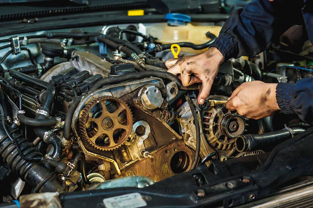 Auto repair technician working on an engine belt and alternator in Naples, FL