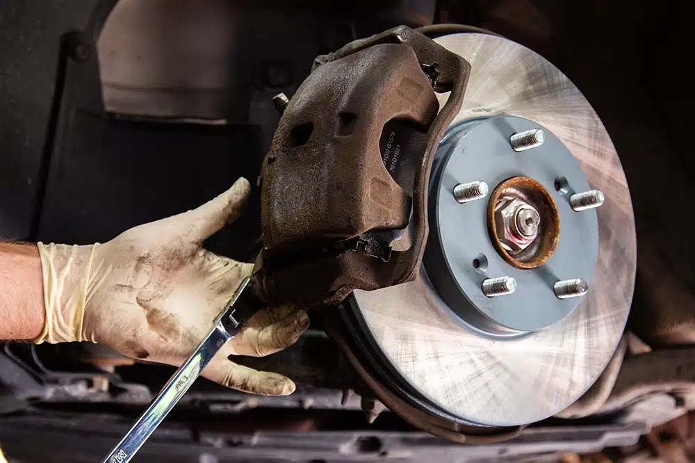 Emergency brake replacement service in Bonita Springs, FL featuring mechanic tightening a brake caliper bolt with a wrench