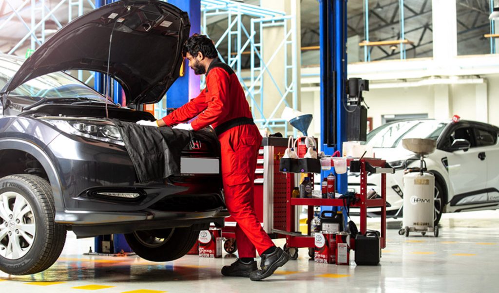 Technician in red coveralls conducting routine vehicle maintenance in a modern auto repair bay in Bonita Springs, FL