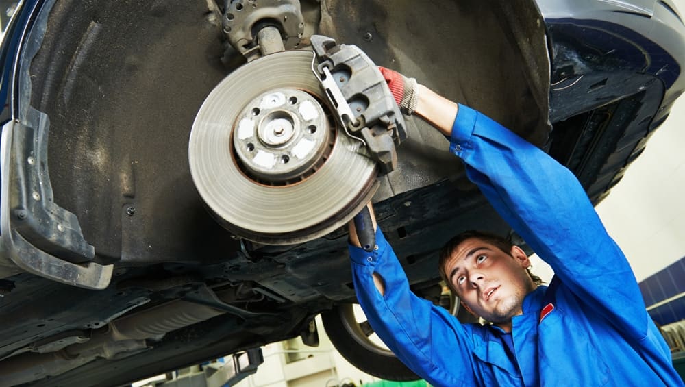 Local auto repair shop technician in Bonita Springs, FL working under vehicle lift performing brake system maintenance