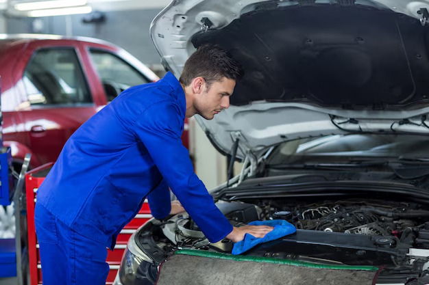 Auto repair shop mechanic in blue uniform cleaning the engine compartment after service in Bonita Springs, FL